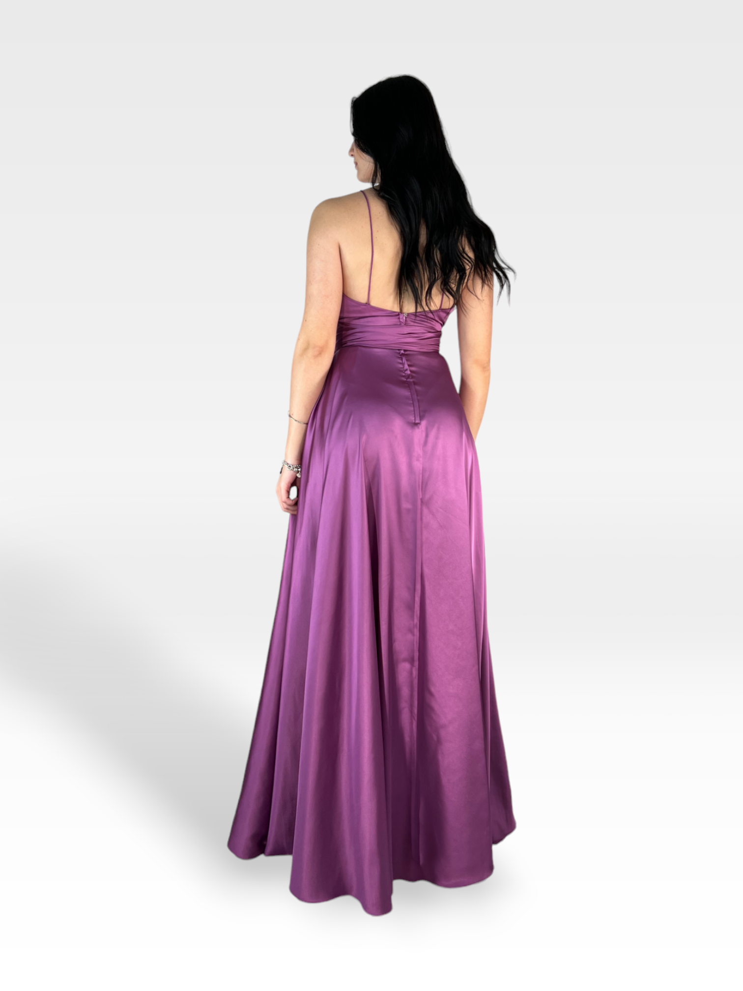 Una donna con lunghi capelli scuri sta dando le spalle alla telecamera, indossando VIOLA 18teen, un abito di raso rosa intenso lungo fino al pavimento con scollo all'americana e un corpetto aderente. Lo sfondo è un semplice grigio chiaro.