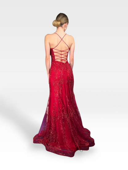 Una donna è mostrata di schiena mentre indossa un abito rosso intenso con intricati dettagli di paillettes. Il TIPHAINE di 18teen presenta un laccio sulla schiena e uno strascico fluido, completato dal suo elegante chignon basso. Lo sfondo è semplice, grigio chiaro.